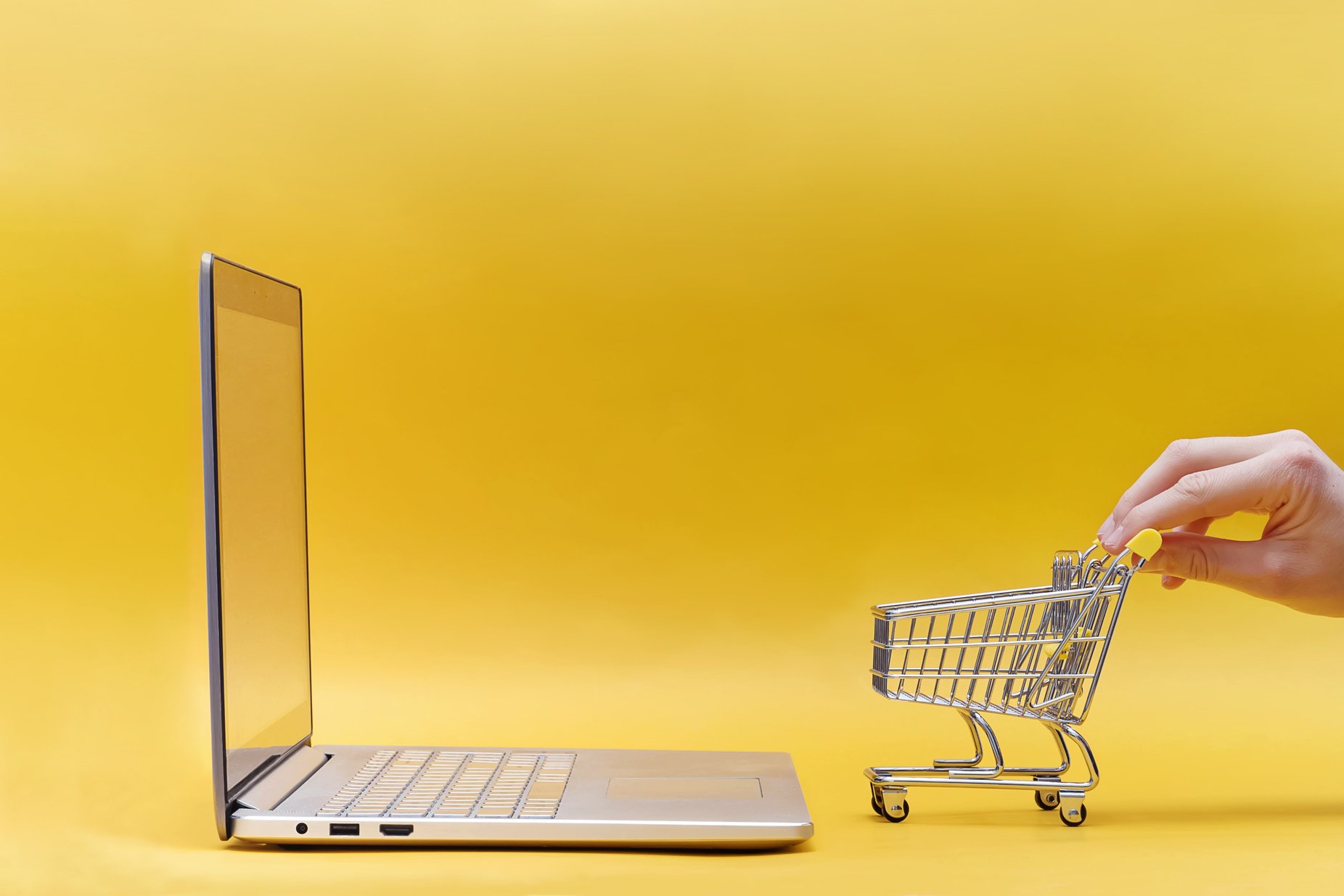 Hand Holding Mini Shopping Trolley near the Opened Laptop